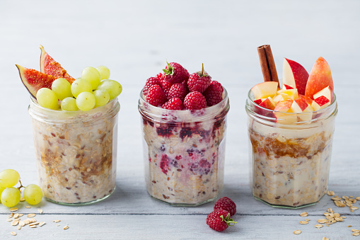 Assortment overnight oats, bircher muesli with fresh berries and fruits in a glass jars on wooden table background. Copy space