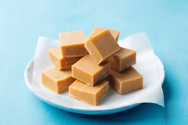 Photo of Fresh caramel fudge candies on a plate. Blue background. Close up.