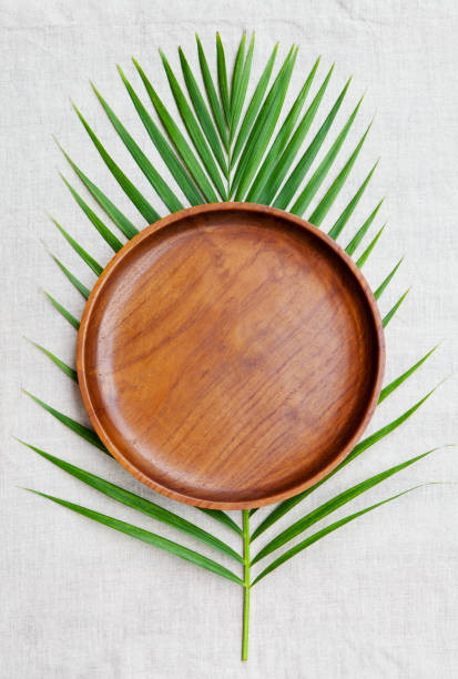 Wooden plate with palm leaf on natural linen textile background. Copy space. Top view