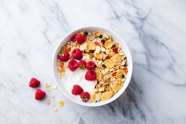 gesundes frühstück. frisches müsli, müsli mit joghurt und beeren auf marmor hintergrund. ansicht von oben. - bran cereal stock-fotos und bilder