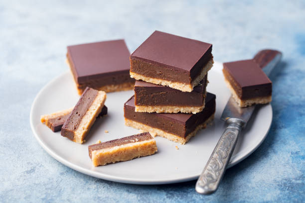 schokolade, karamell scheiben, bars, millionäre shortbread auf einer grauen platte. blauer hintergrund. hautnah. - shortbread caramel chocolate candy biscuit stock-fotos und bilder