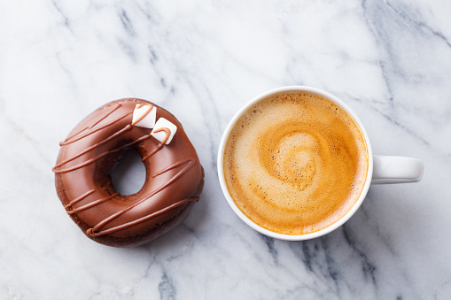 Coffee with chocolate donut in marble table background. Top view