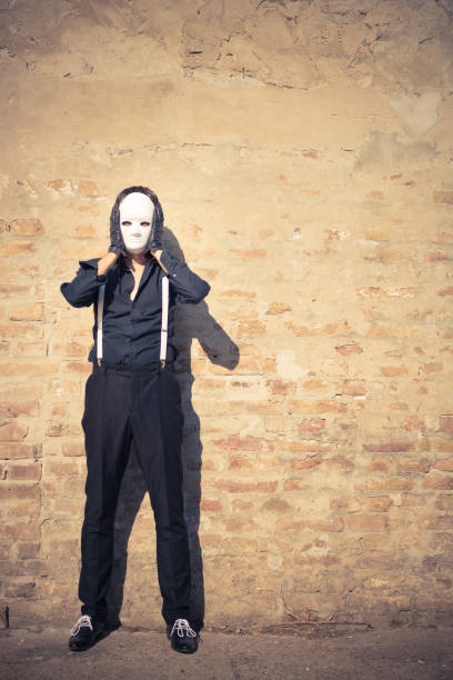 Man in black standing against the wall and hiding face with mask. Copy space.