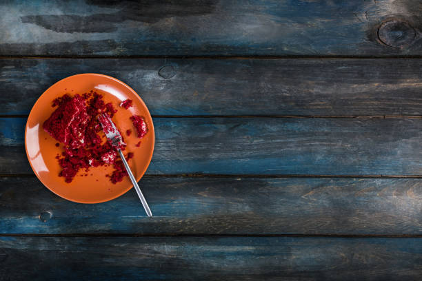 Top View. In the process of eating delicious Red velvet cake on a ceramic plate with a fork on a colored wooden background