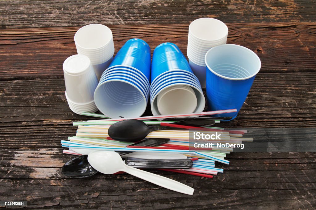 Disposable plastic straws, cups, cutlery Plastic straws and twizzle stirring sticks, plastic cups in various sizes, plastic cutlery.  Single use plastic items, environmental issue, plastic pollution. Plastic dining or party supplies. Plastic Stock Photo