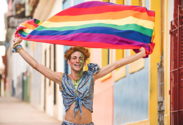 homme gay en cours d’exécution tenant le drapeau arc-en-ciel - gay pride rainbow flag homosexual photos et images de collection