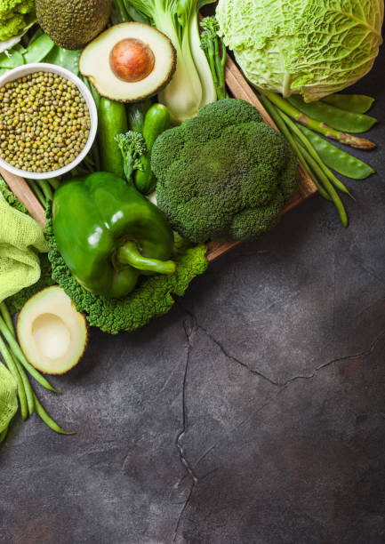 istock Assorted green toned raw organic vegetables on dark background. Avocado, cabbage, broccoli, cauliflower and cucumber with trimmed beans. Space for text 1126957914