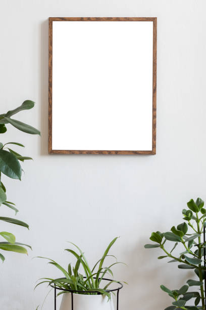 istock Scandinavian and botanical interior with brown mock up poster frame on the white wall. White backgrounds walls. Modern and floral concept. Nature lover. 1126958904