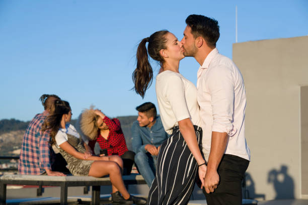 A Latin couple between 20-30 years showing their love and sharing with friends on the rooftop terrace