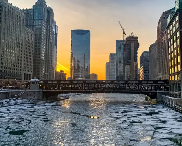 Photo of Sunset glow reflects off of windows of skyscrapers and ice on the surface of an icy Chicago River during winter evening