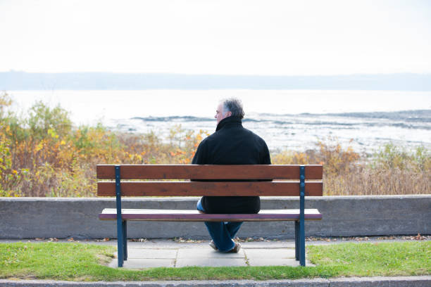 istock Mature man sitting on park bench overlooking river. 1126966898