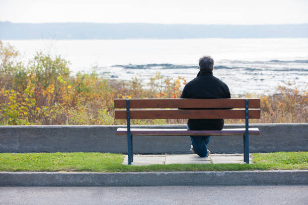 A man seated on a wooden bench by a tranquil lake