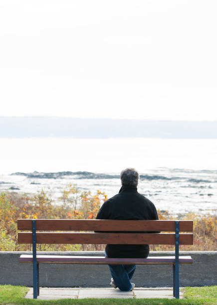 istock Mature man sitting on park bench overlooking river. 1126966911