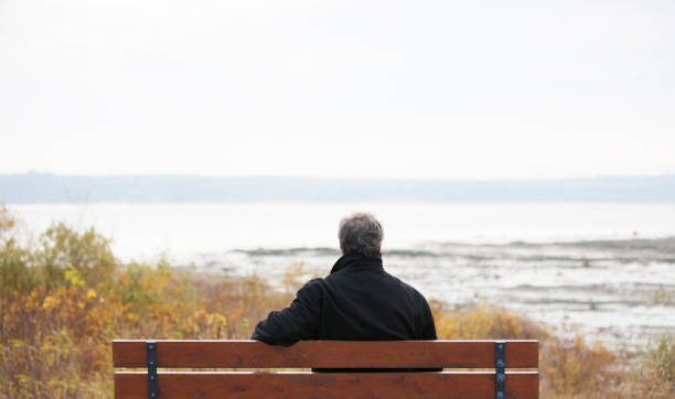 istock Mature man sitting on park bench overlooking river. 1126966931