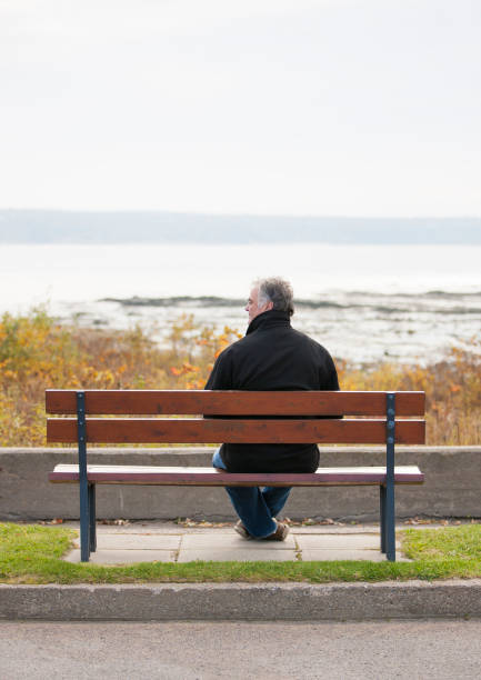 istock Mature man sitting on park bench overlooking river. 1126966950