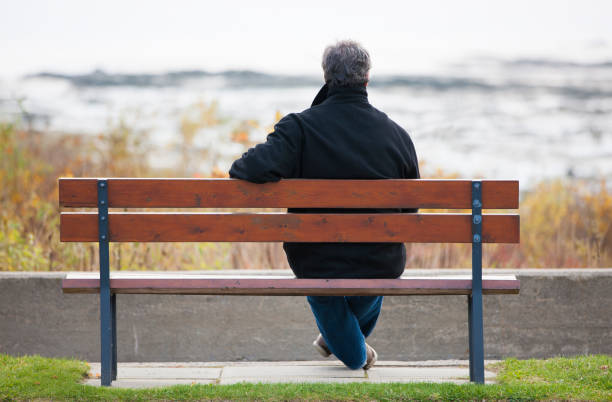 istock Mature man sitting on park bench overlooking river. 1126966955