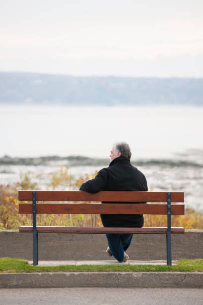 istock Mature man sitting on park bench overlooking river. 1126966969