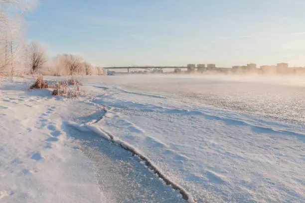 Winter landscape in the early morning overlooking the city of Dubna and the bridge over the Volga. Frosty fog obscures the banks of the river. The tops of the trees are covered with hoarfrost.