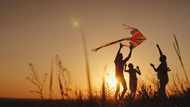 feliz familia jugando con una cometa al atardecer. mamá, papá e hija son felices juntos - cometa fotografías e imágenes de stock