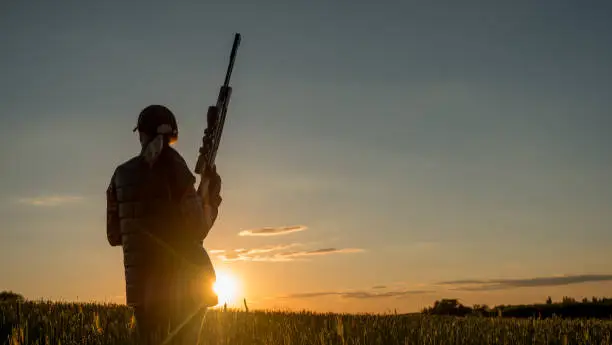 Beautiful silhouette of a woman with a rifle in the rays of the setting sun. Sports shooting and hunting concept. 4K video