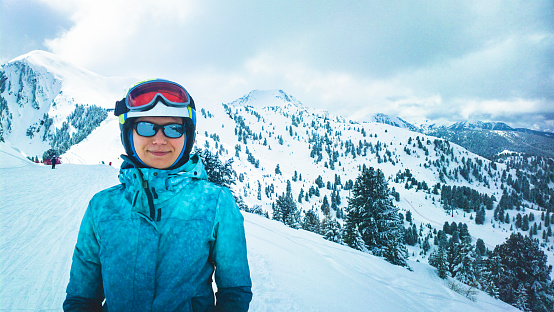 Woman with ski helmet, goggles and sunglasses in snow covered mountains.