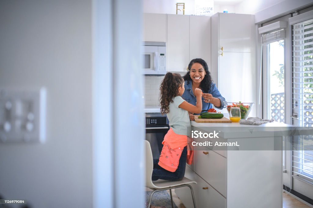 Mother and daughter cooking food in kitchen Smiling mother cutting bell pepper at kitchen island. Woman and daughter preparing food together at home. They are representing healthy lifestyle. Family Stock Photo