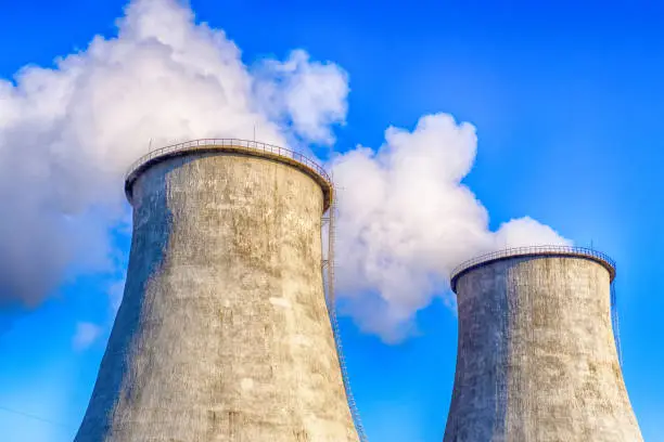 Two big smoking pipes of powerplant. Heavy white smoke on blue sky background.