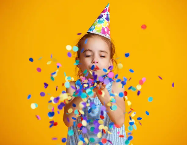 Photo of happy birthday child girl with confetti on yellow background