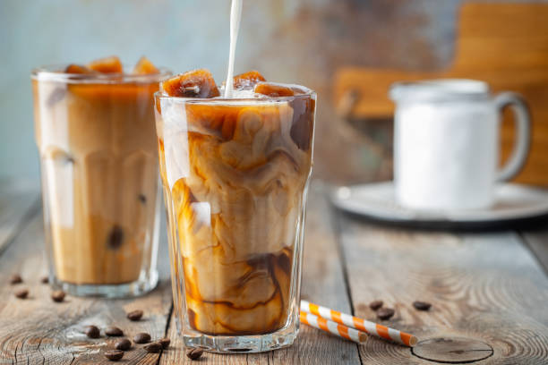 istock Ice coffee in a tall glass with cream poured over, coffee ice cubes and beans on a old rustic wooden table. Cold summer drink with tubes on a blue rusty background with copy space 1126996366
