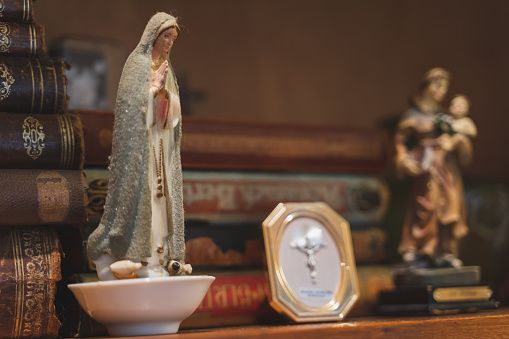 Statue of Mary, mother of Jesus, according to the New Testament and the Quran sitting on an old shelf filled with very old books.