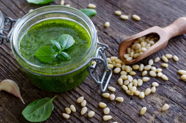 Pesto genovese - traditional Italian green basil sauce with pine nuts, basil and garlic on rustic wooden background.