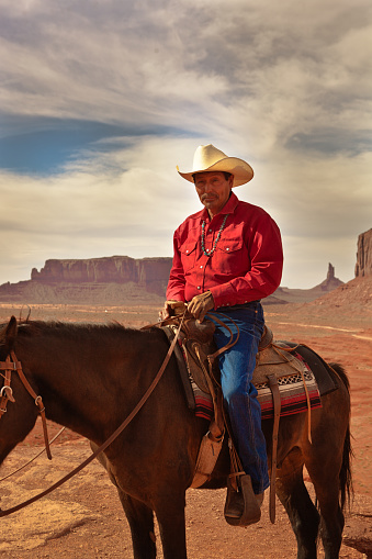 Portrait of a native American cowboy on horseback at the Monument Valley Tribal Park in Arizona, USA. A famous tourist destination in the southwest USA. The iconic western landscape is a backdrop for many western movies. The native American is a Navajo tribe native. Photographed on location.