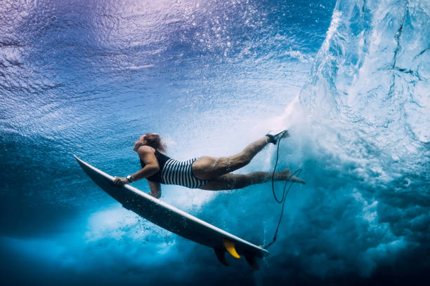 istock Surfer woman with surfboard dive under wave 1127028055