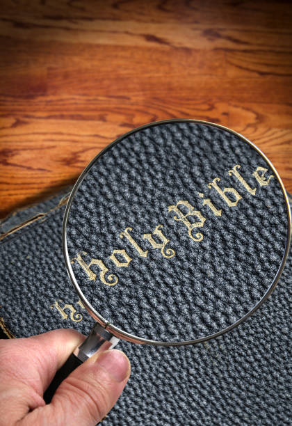 рука, держащая увеличительное стекло над старой священной библией с пространством копирования - magnification bible magnifying glass book стоковые фото и изображения