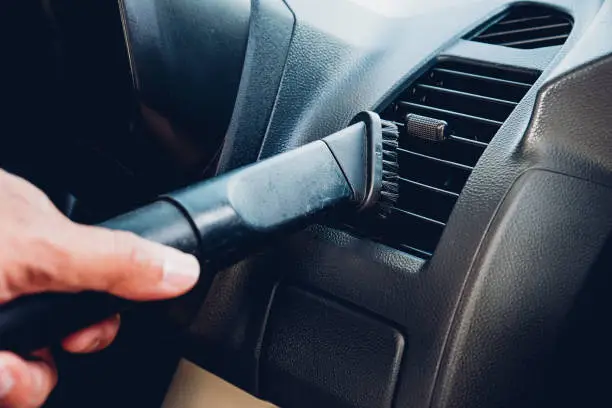 Worker man cleaning dust interior vacuum inside car after wash
