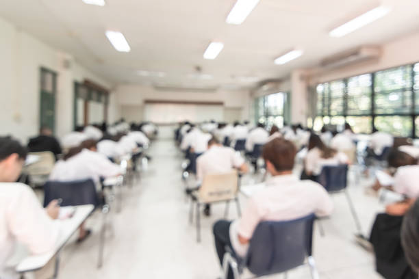 Blur school student exam background  in university class with blurry view from back of the classroom of young people having stress doing examination admission test in classroom for education
