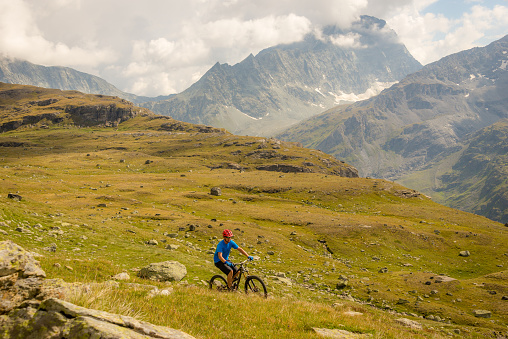 A man riding a mountain bike along a trail in the Alps with glaciers and mountain peaks in the background.