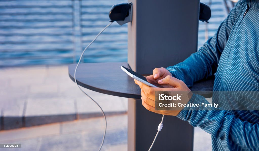 Female charging phone on a public charger Female using phone and charging on a public charger Charging Stock Photo