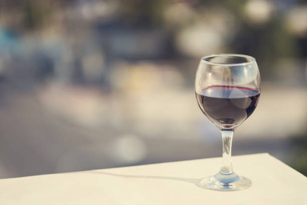 close up of glass of red wine against the background of blurred town with bokeh at summer evening - sky sea town looking at view imagens e fotografias de stock