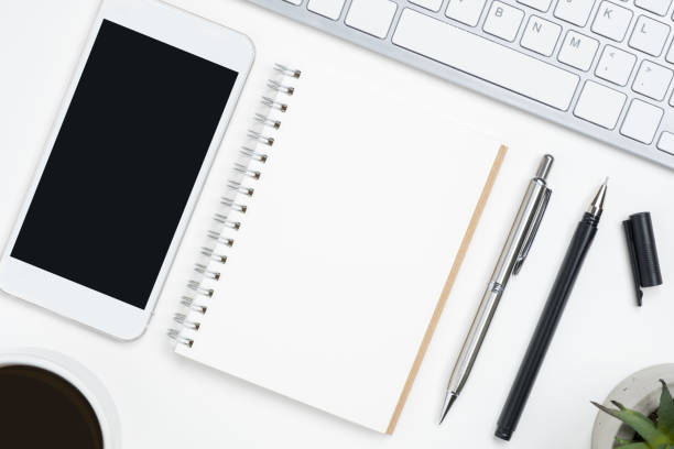 istock Blank notebook and mobile phone with blank mockup screen are on top of white office desk table. Top view, flat lay. 1127062011