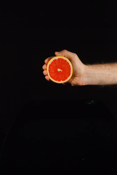 istock Half of a juicy grapefruit in man's hand on black background 1127066795