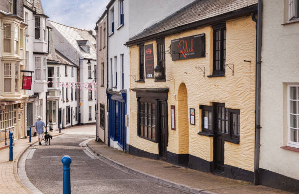 14 June 2017: Ilfracombe, North Devon, England, UK - A man walks with his greyhound down Fore Street, formerly the most important street in the town, passed traditional terraced cottages.