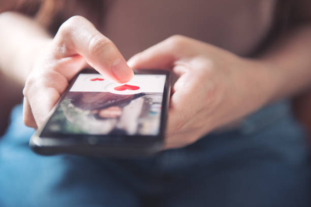 палец женщины толкает значок сердца на экране в мобильном приложении смартфона. онлайн знакомства приложение, день валентина концепции. - свидание стоковые фото и изображения