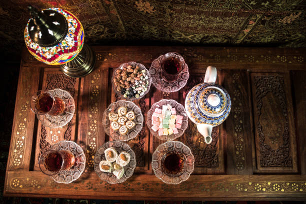 istock Arabian tea in glass with eastern snacks on vintage wooden surface. Eastern tea concept. Low light lounge interior with carpet. Empty space. 1127087230