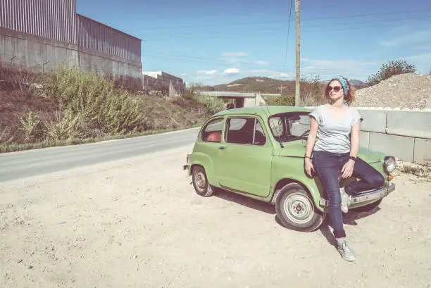 A ginger girl sitting on the side of her restorated green supermini automobile
