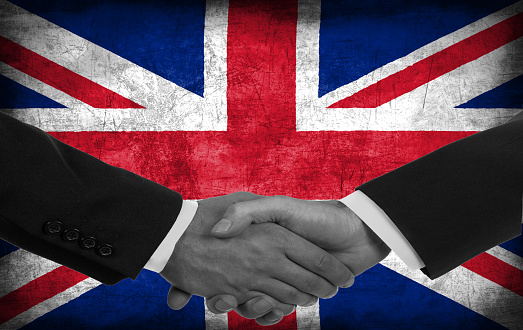 Two men/politicians in suits shaking hands with the national flag on the background - United Kingdom