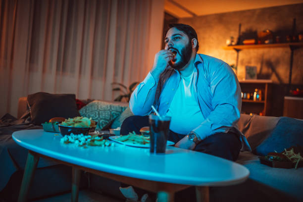 istock Fat man eating fast food and watching TV 1127093057