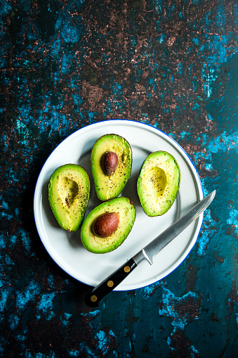 Color image depicting an overhead view of fresh avocados. The avocados have been cut in half and are presented on rustic surfaces with plenty of room for copy space.