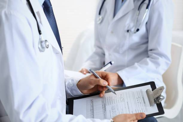 istock Two unknown doctors filling up medical form on clipboard, just hands closeup. Physicians asking question to patient or discussing medication program. Healthcare, insurance and medicine concept 1127093909