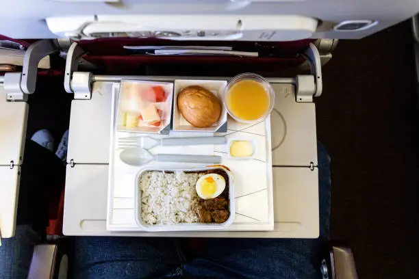 Overhead view of basic inflight meal of economy class consisting rice, egg, beef curry, bread, fruits, and juice.